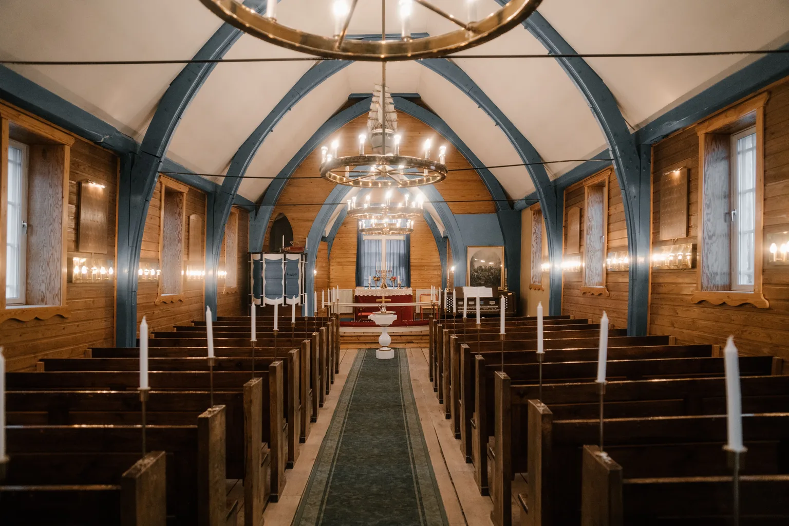 Wooden pews lining a center aisle runner in a warmly lit sanctuary