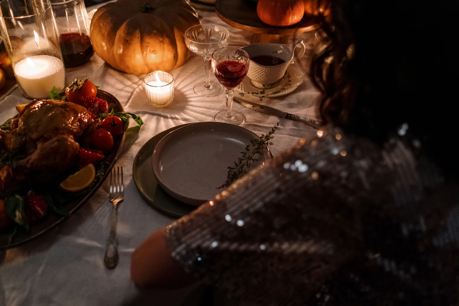 A holiday dinner table set with candles, plates, and serving dishes in warm light