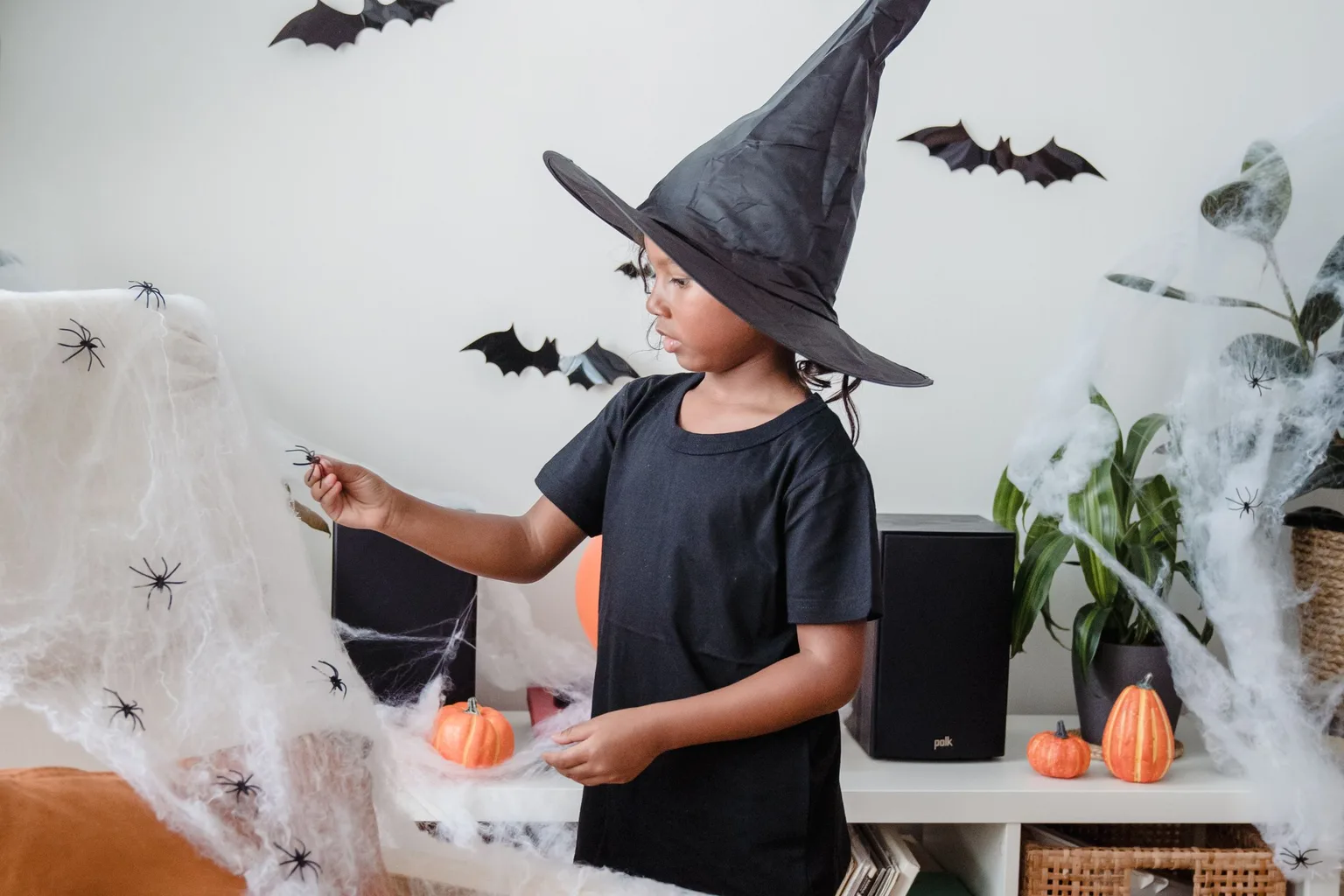 A young girl in a witch hat in a room decorated for Halloween