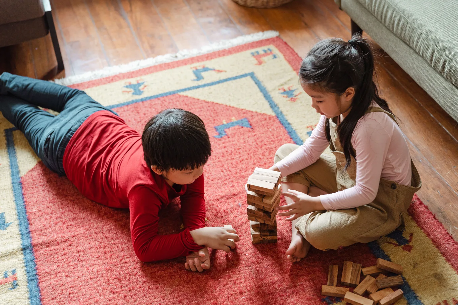 Two young children playing with wooden blocks on a rug in a living room
