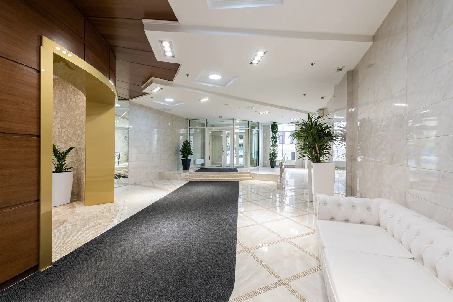 A bright professional lobby with a long carpet runner leading across polished tile to glass entry doors