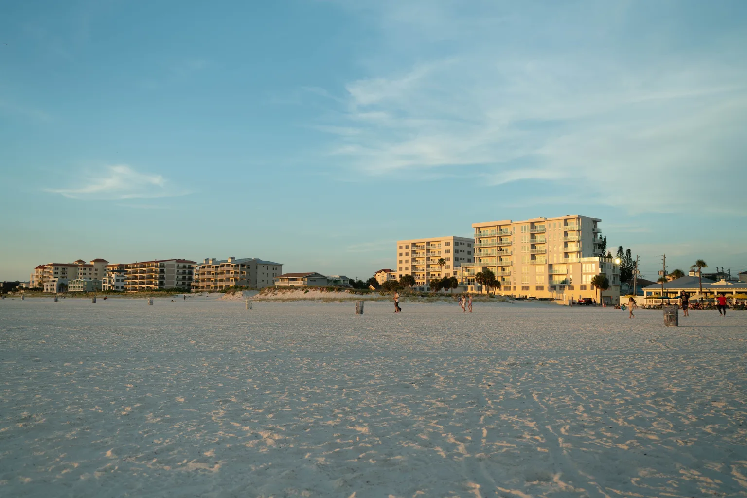 Beachfront condominium buildings behind an empty stretch of sand at sunset