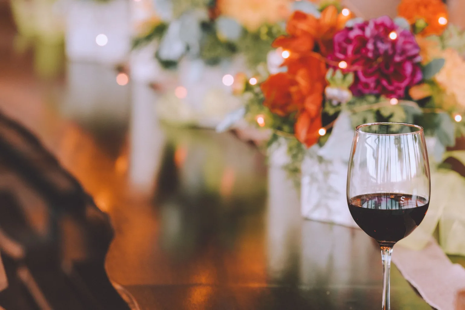 A glass of red wine served on a wooden table with flowers