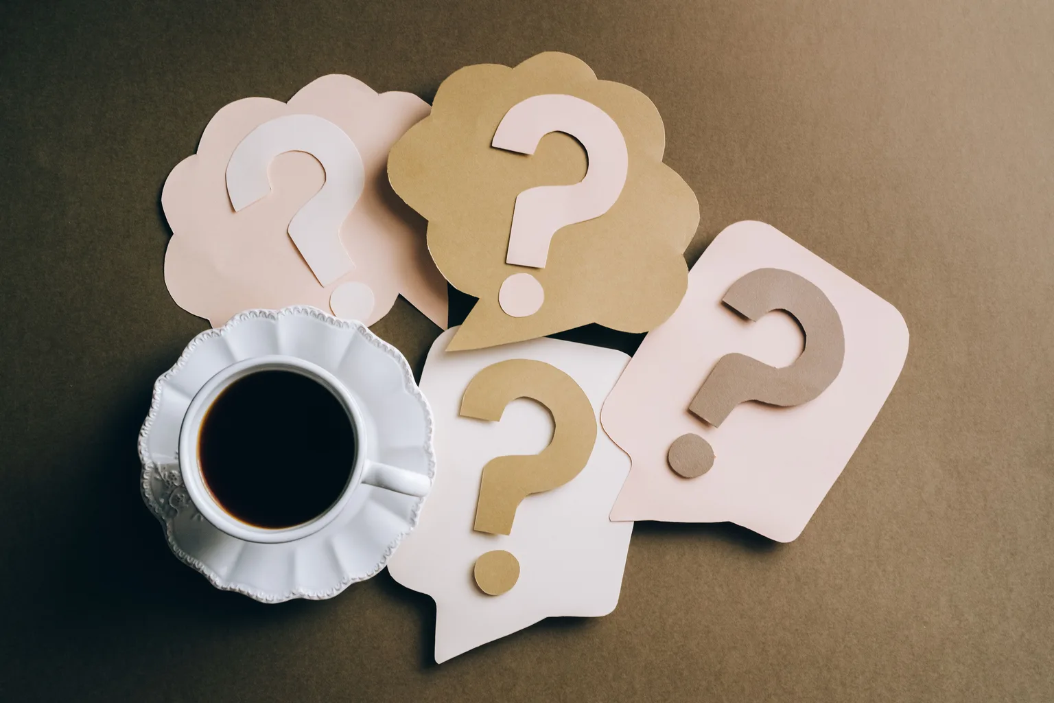 Paper question marks arranged on a table beside a coffee cup